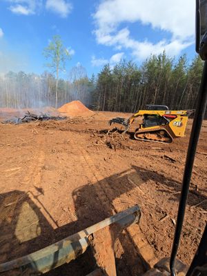 A bulldozer clearing land, with smoke in the distance. The sky is blue and the ground is brown.