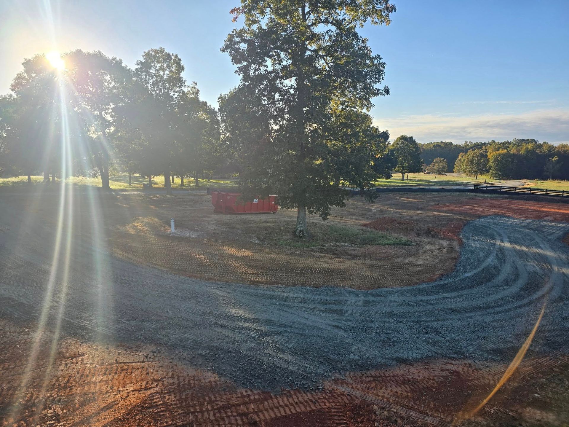 Sun shining over gravel driveway, dirt, and trees on a sunny day.