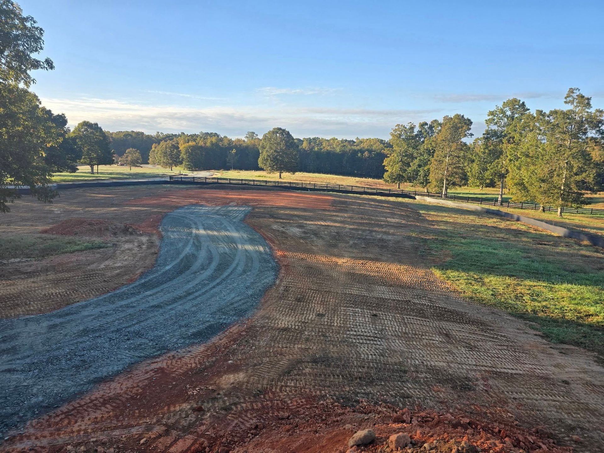 Gravel driveway curves through a construction site, leading toward trees and a blue sky.