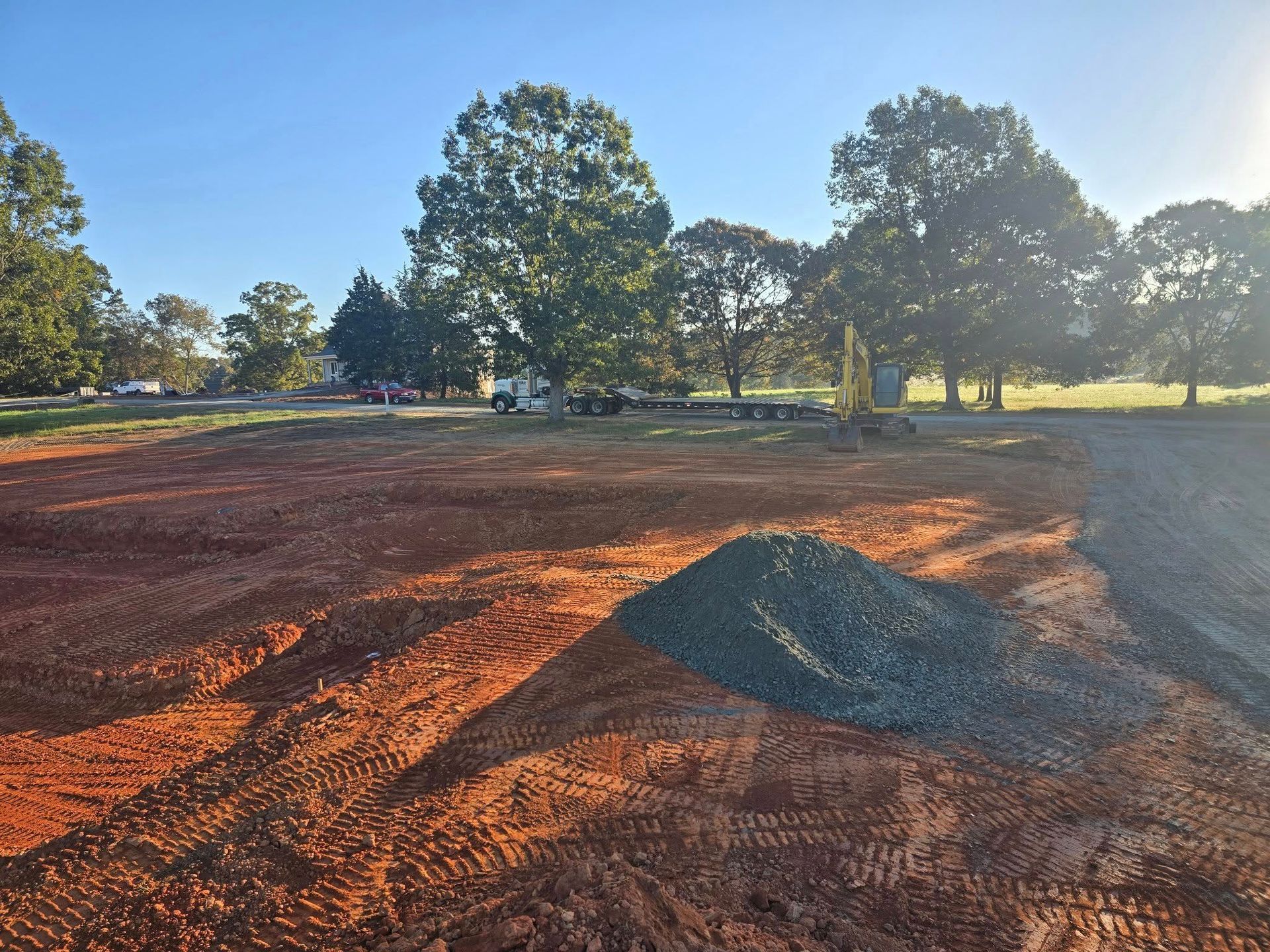 Red earth cleared for construction with a pile of blue gravel; trees and a bright sky in the background.