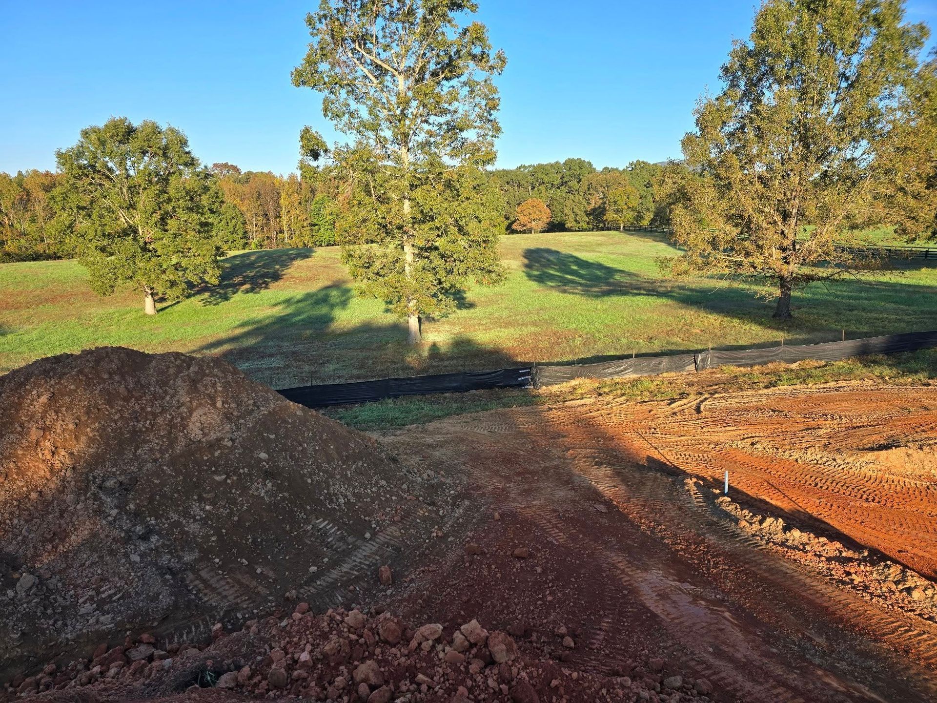Earthen mounds in foreground with grassy hills and trees under a clear blue sky.