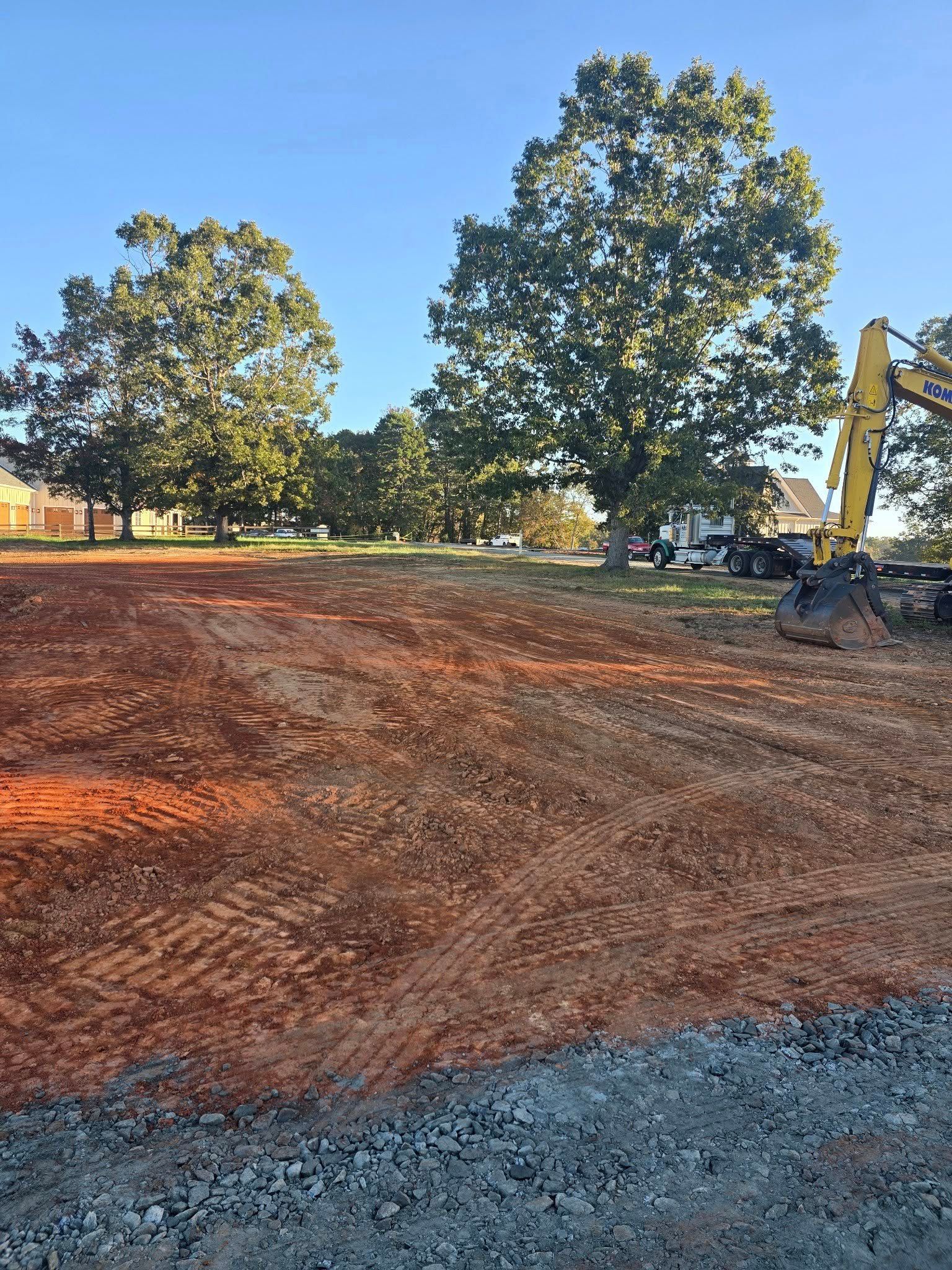 Cleared dirt lot with red soil and trees in background. Construction equipment visible.