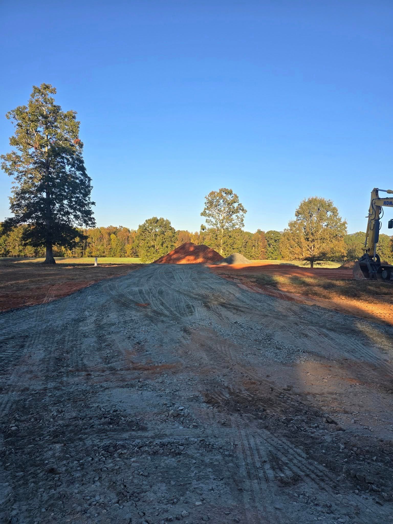 Pile of gravel in foreground, trees and blue sky in background. Construction site.