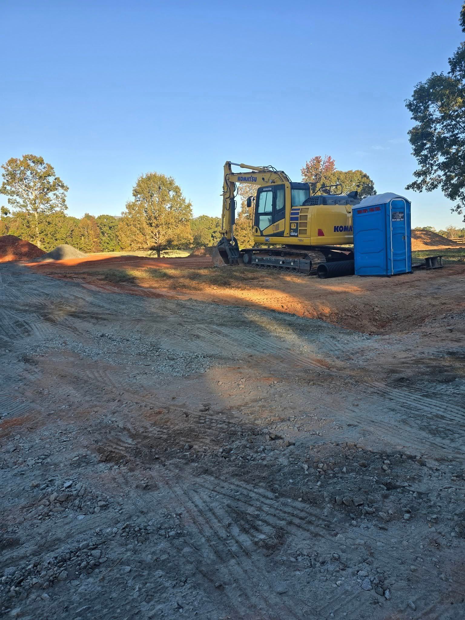 Yellow excavator and blue portable toilet on a construction site, with a clear sky.