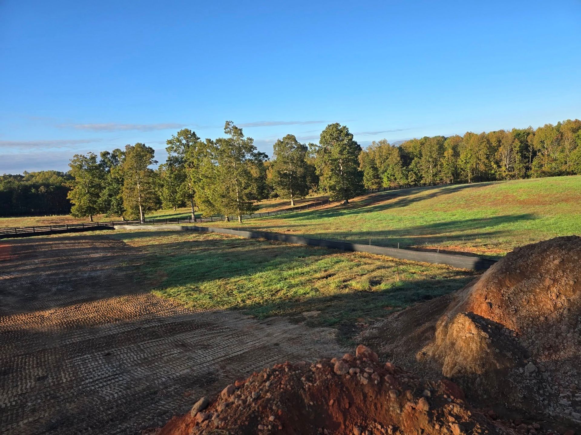 Construction site with graded earth, grass, trees, and blue sky.