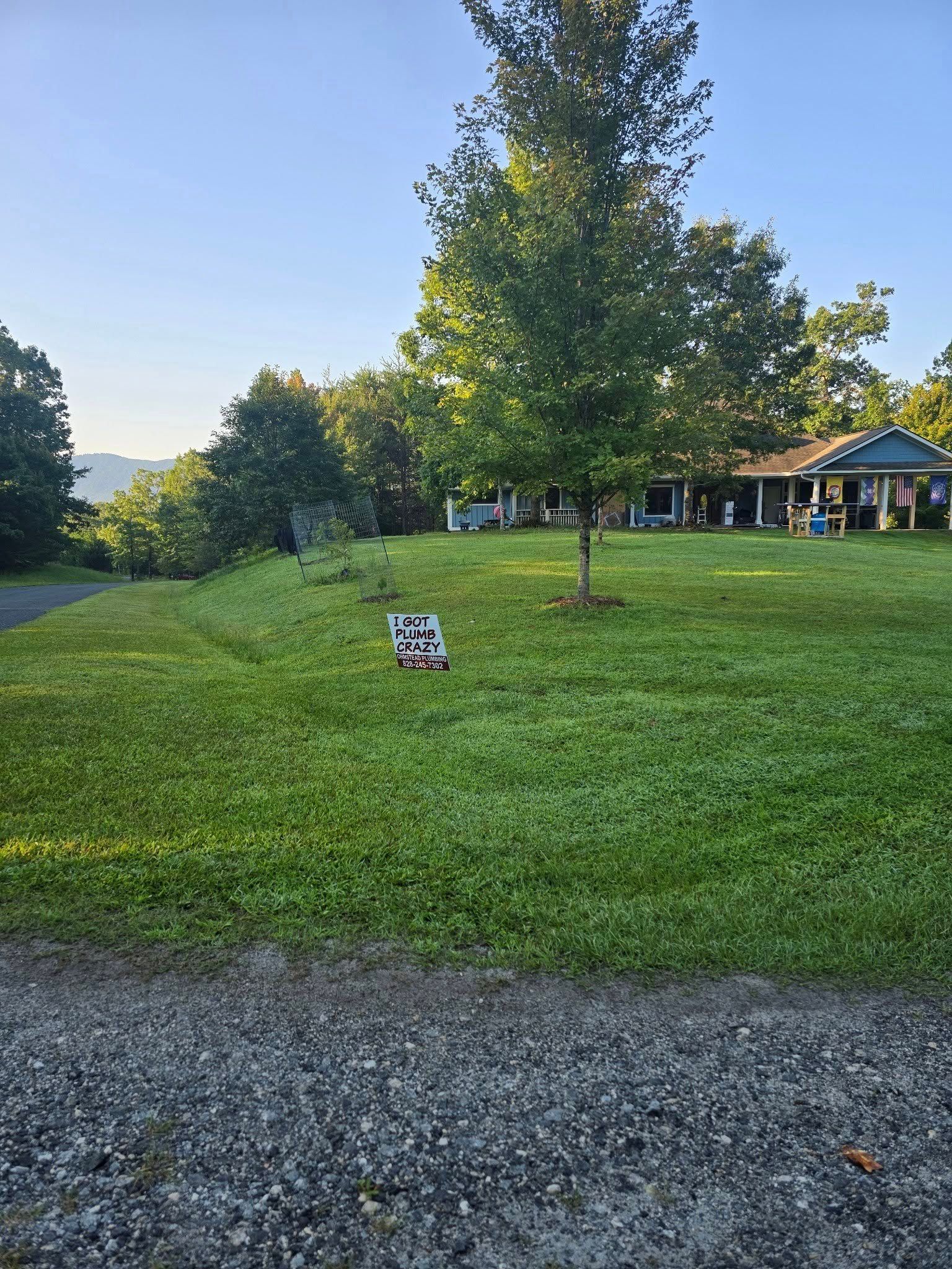 Green lawn with trees and a house, a sign stands in the grass.