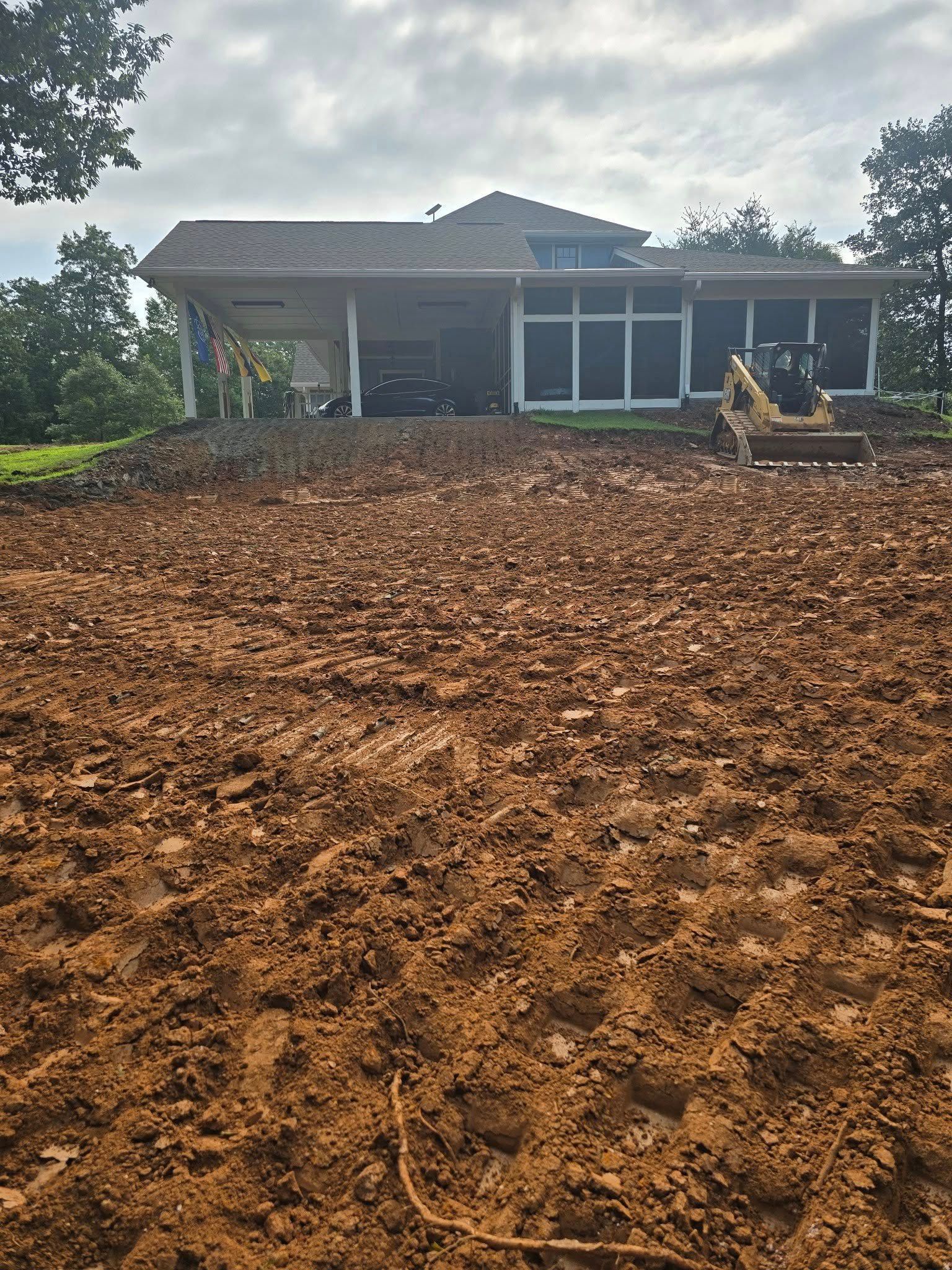 Dirt work in front of a house, possibly for landscaping. An excavator is present. Overcast sky.