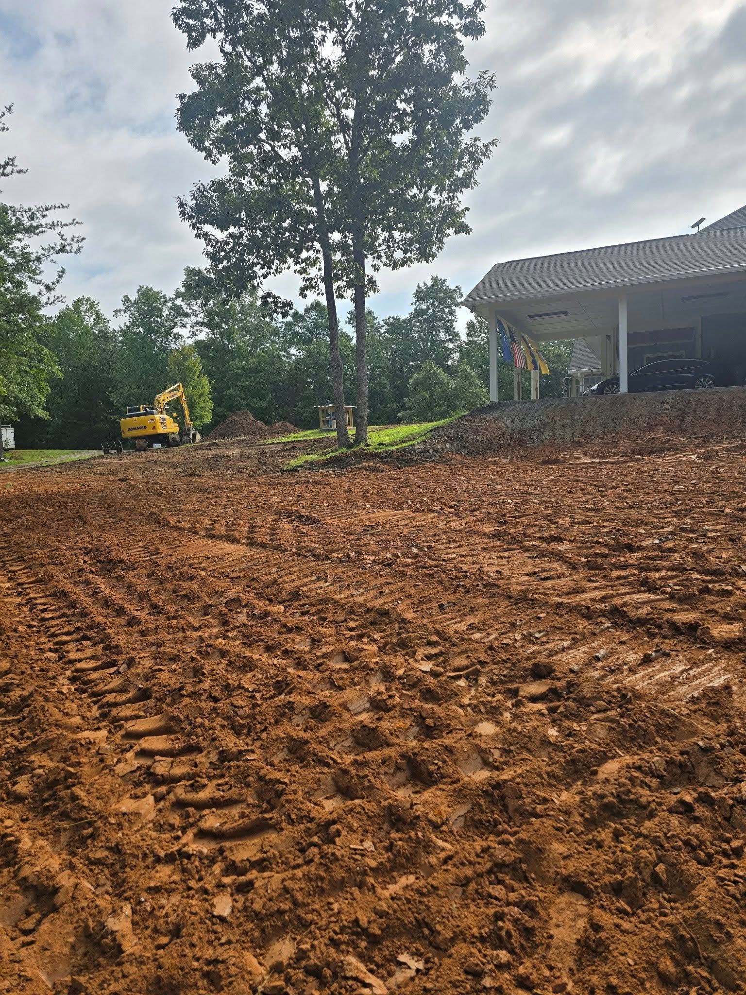 Muddy construction site with an excavator and a partially built structure in the background under a cloudy sky.