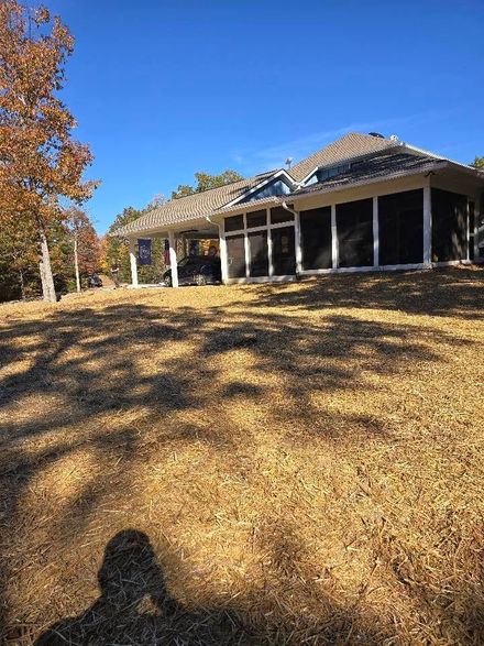 A low-slung house with a dark facade, set on a grassy hill under a bright blue sky.