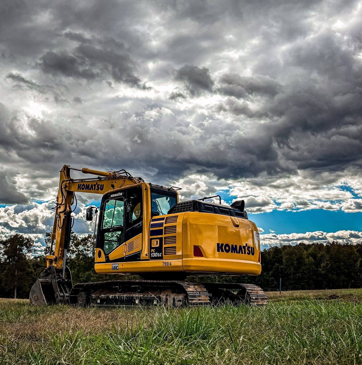 Yellow Komatsu excavator on grass field under cloudy sky.