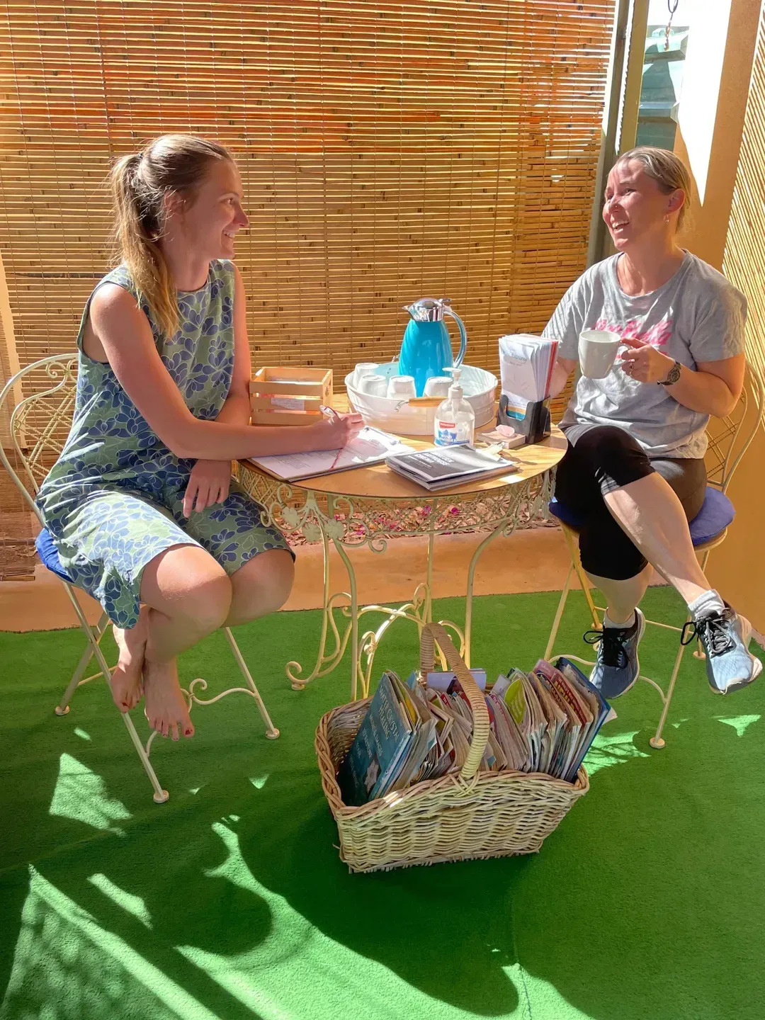 Two women are sitting at a table with a basket of books. — Aloha Therapeutic Massage In Gillen, NT