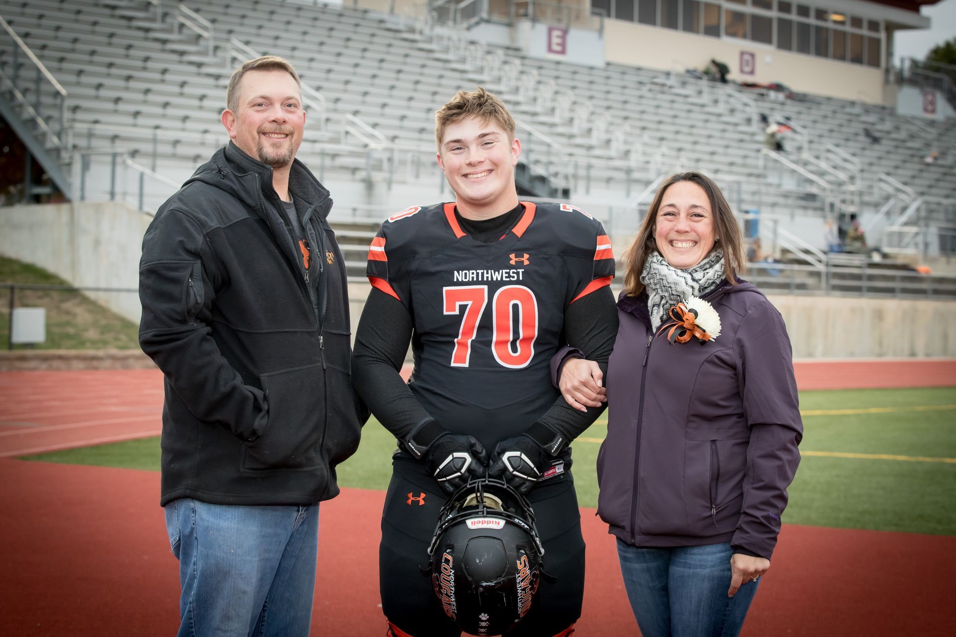 A football player is posing for a picture with his parents on a field.