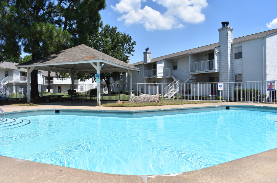 Aerial view of apartment complex with carports, brown roofs, green trees, and a pool.