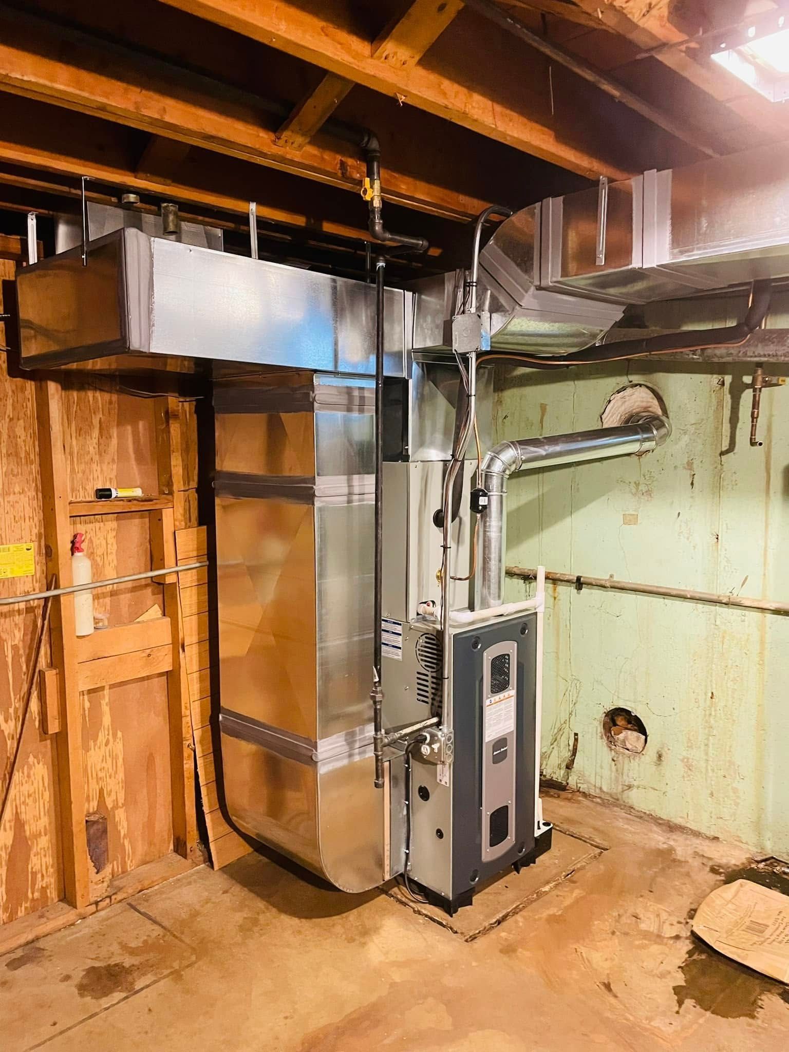 Basement furnace and ductwork beside unfinished wooden walls and exposed ceiling joists
