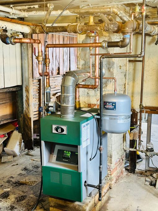 Utility room with exposed plumbing and a silver water heater beside a gray tank on a concrete floor.