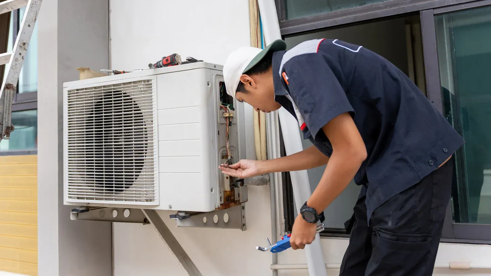 Technician repairing an outdoor air conditioner unit beside a wall.