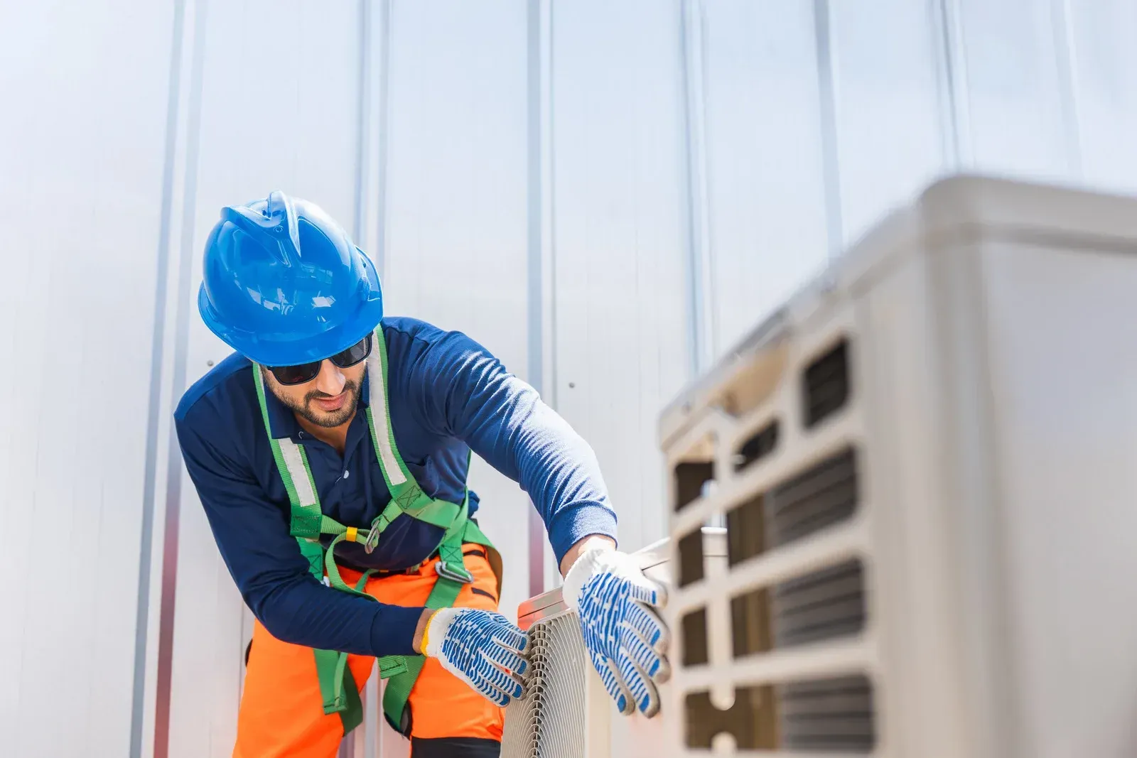 Worker in blue hard hat and orange vest adjusting equipment beside an HVAC unit indoors