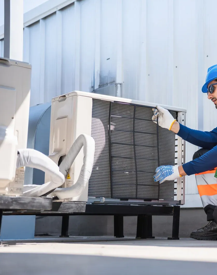 Worker in blue hard hat handling an outdoor air conditioner unit beside a building.