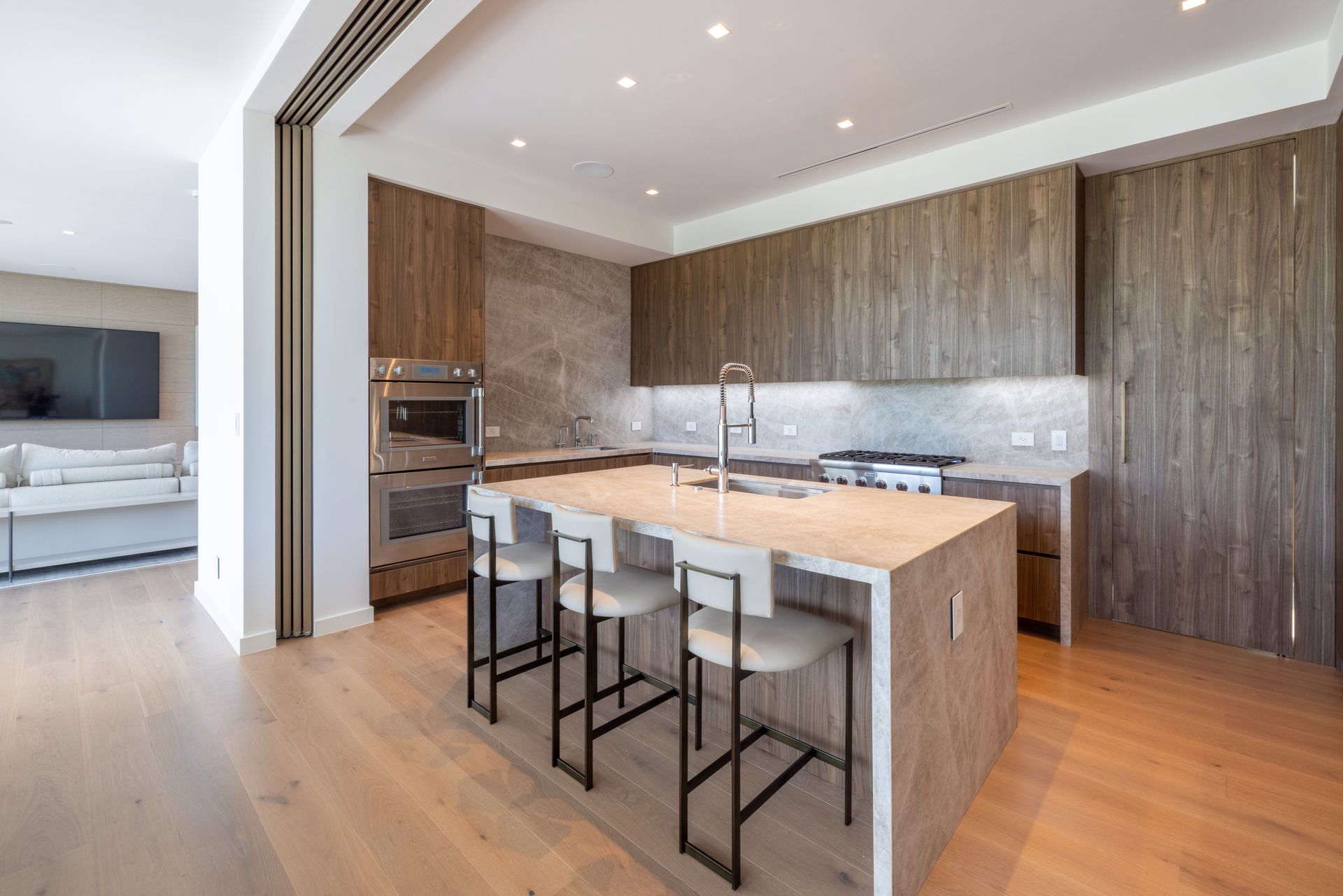 Modern kitchen with island, wood cabinets, stainless steel appliances, and bar stools.