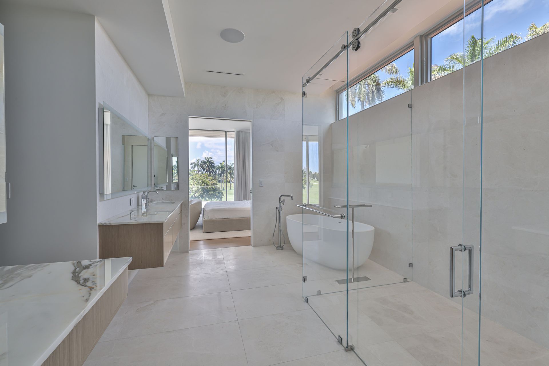 Spacious, modern bathroom with a freestanding tub, glass shower, and marble countertops, with view of the outside.