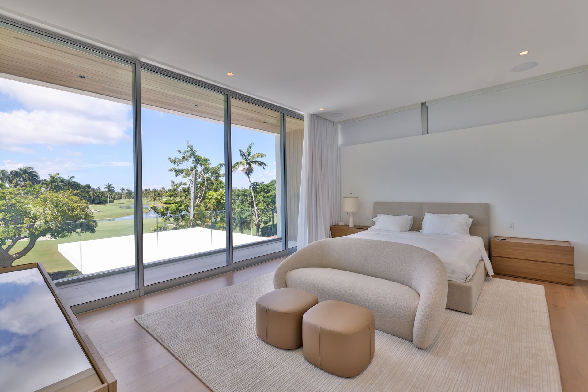 Bedroom with large windows overlooking a golf course. White walls, beige sofa, and a fluffy rug.