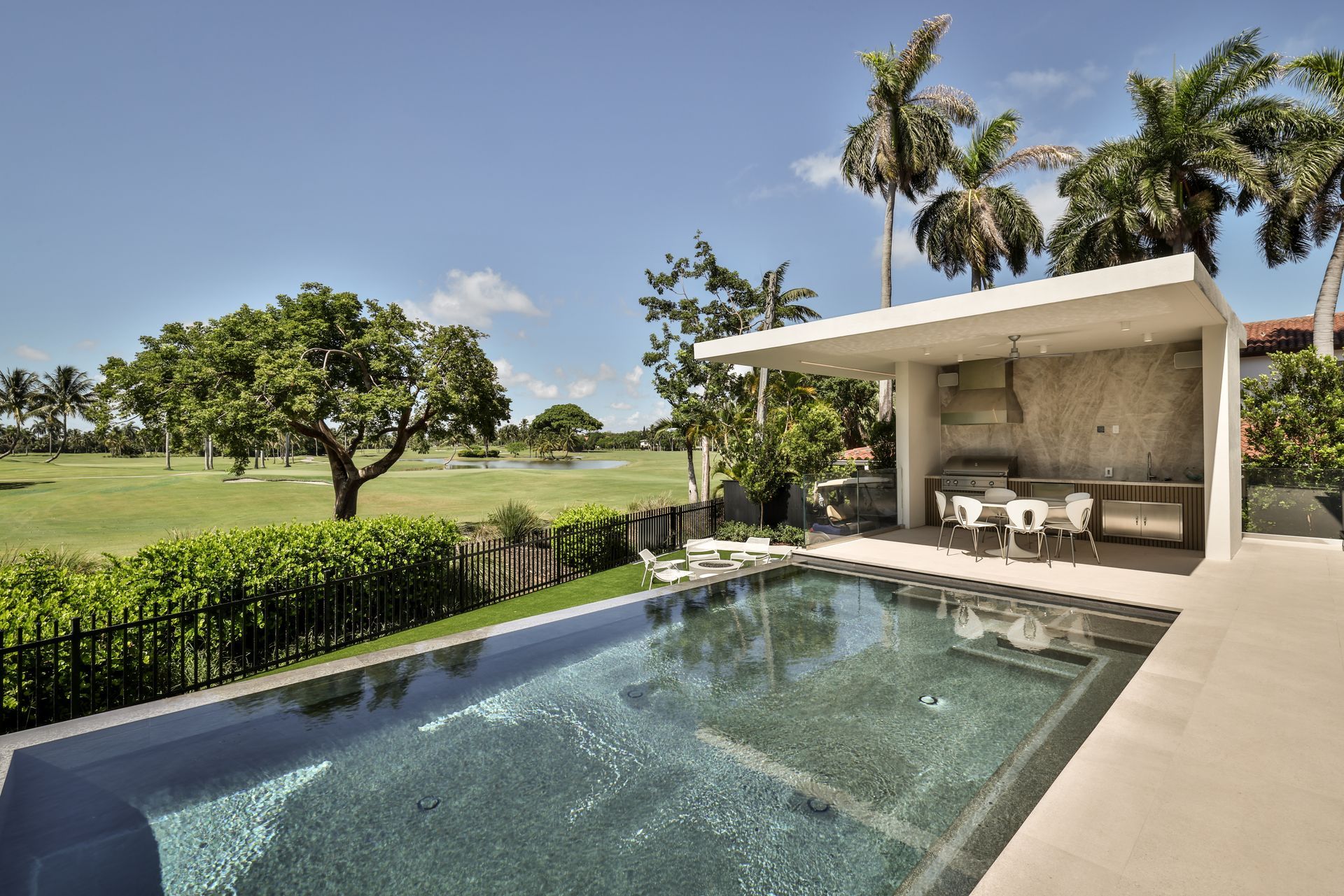 Poolside patio with a view of a golf course and palm trees under a blue sky.
