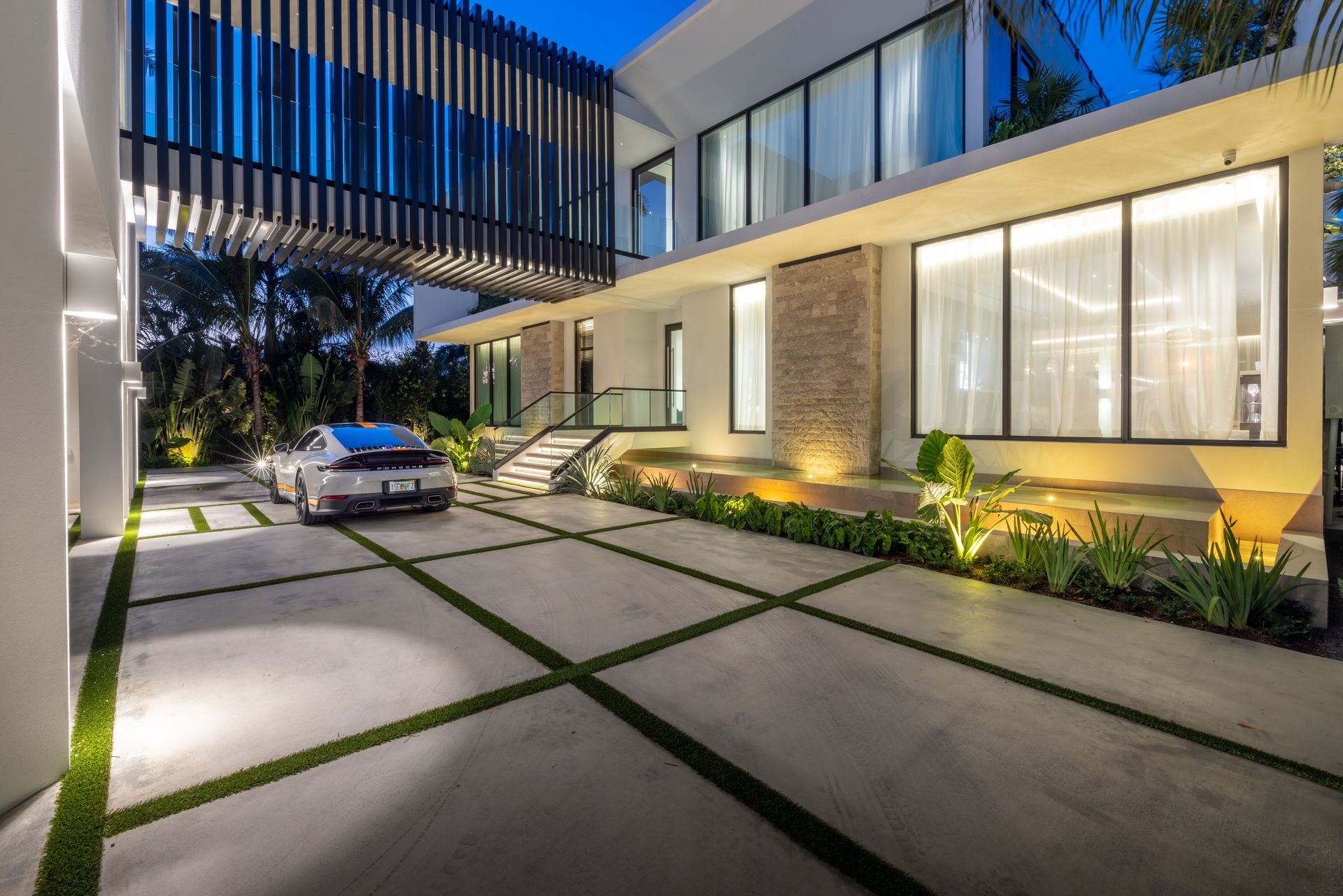 Modern white house with illuminated features, Porsche in driveway, at dusk.