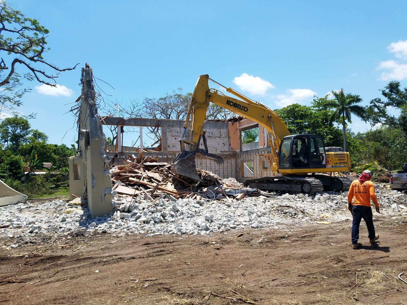 A large yellow excavator is demolishing a building in a field.