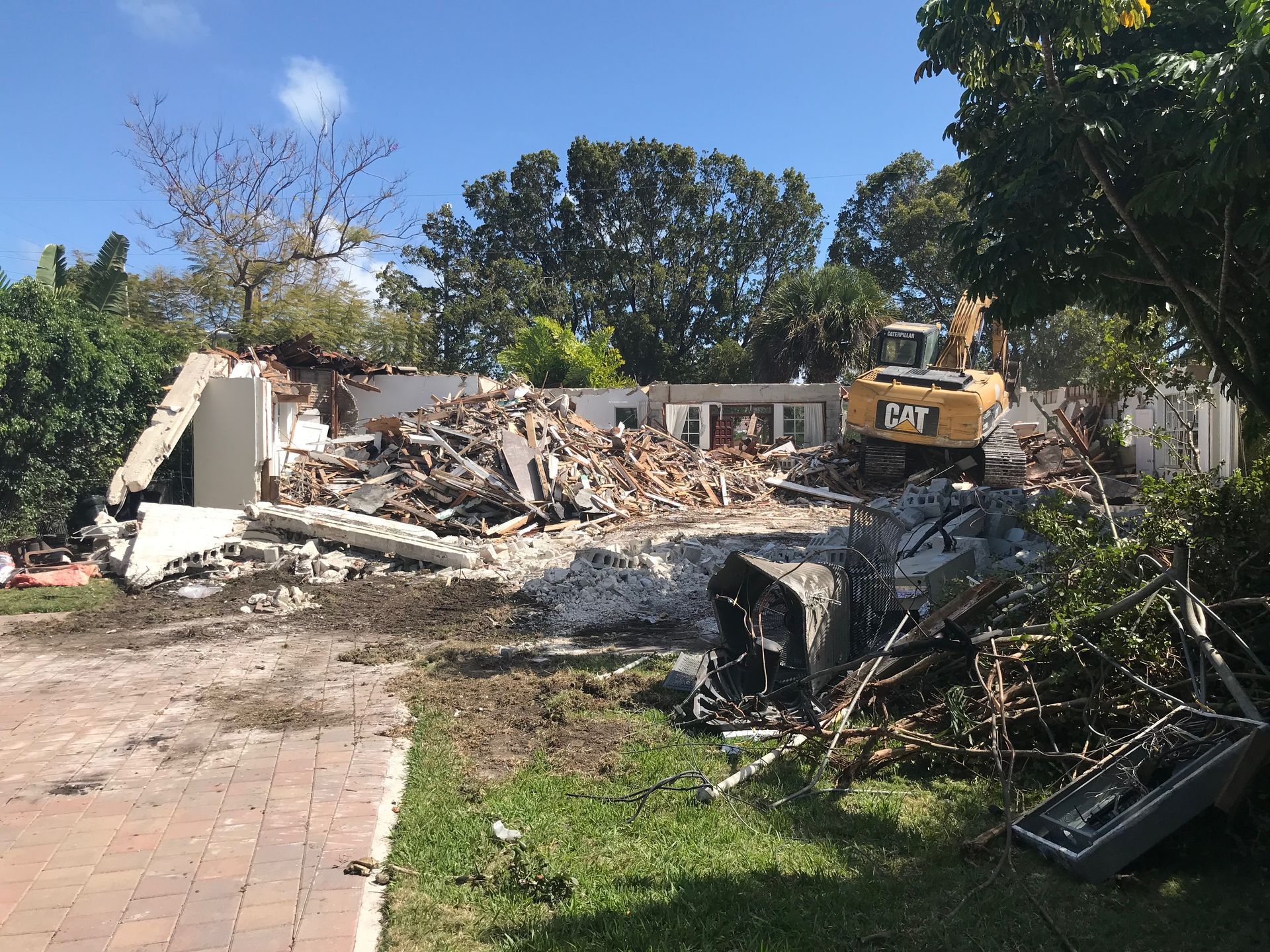 Demolished building with an excavator. Debris and rubble on the ground, trees in the background.