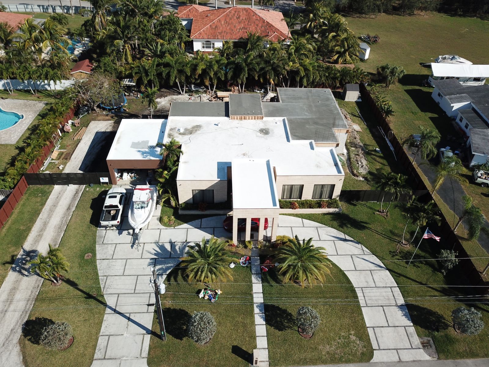 An aerial view of a house with a boat, driveway, and palm trees.