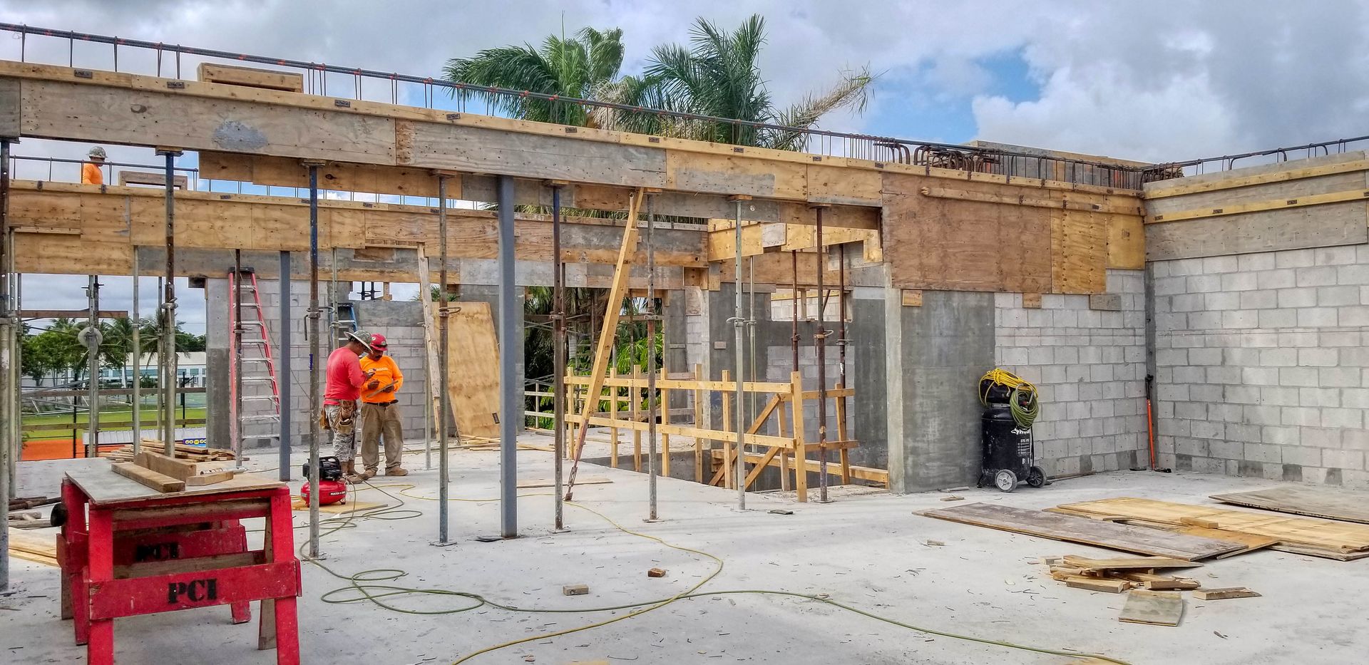 Construction site with workers, wooden beams, concrete blocks, and a cloudy sky.