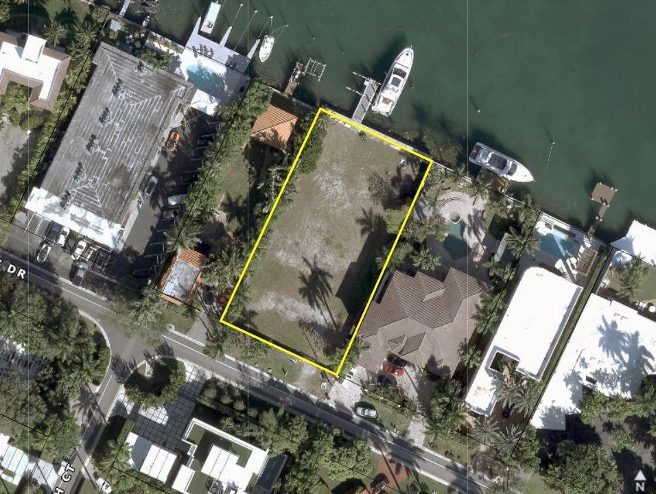 Aerial view of vacant waterfront lot outlined in yellow, near boats and buildings.