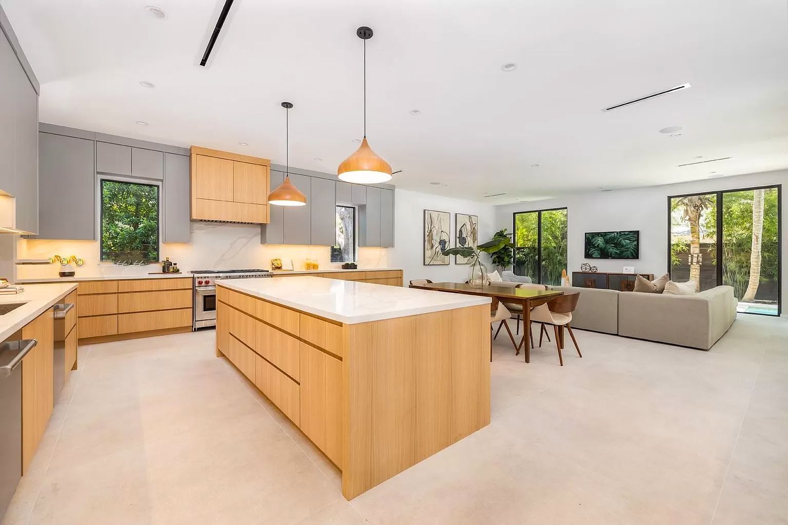 Open-concept kitchen and living area with light wood cabinets, gray walls, white countertops, and large windows.