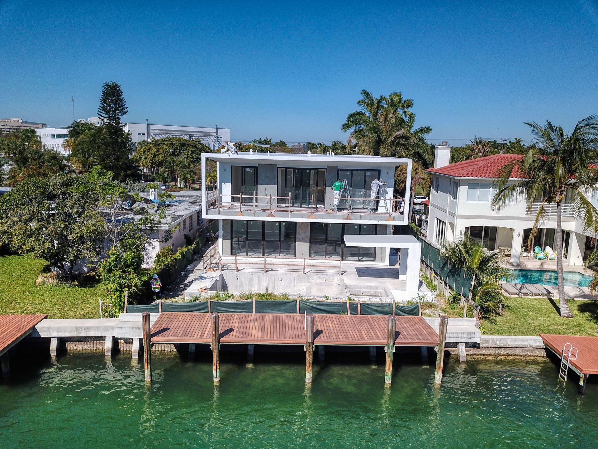 Modern two-story house with dock on water, featuring a white exterior and dark glass windows.
