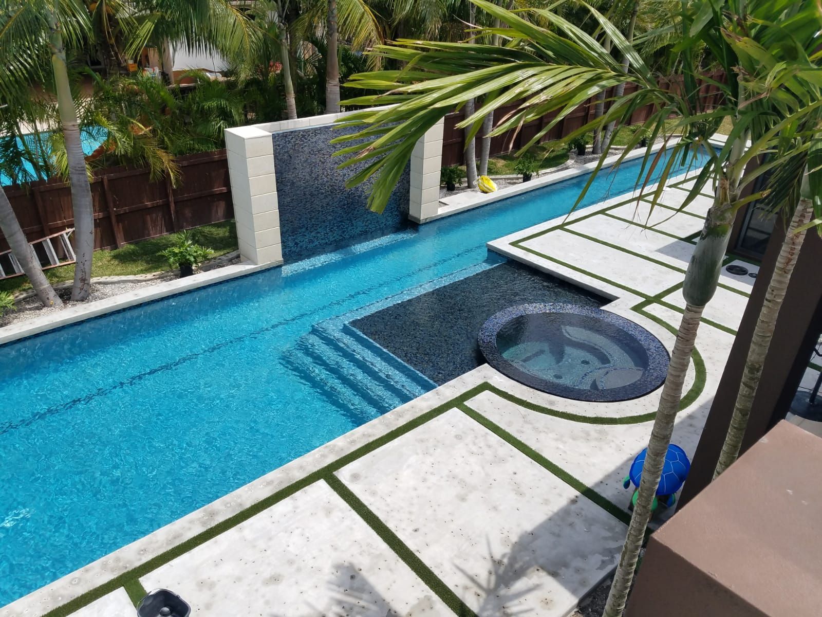 Long, narrow turquoise pool with waterfall feature, spa, and concrete patio.