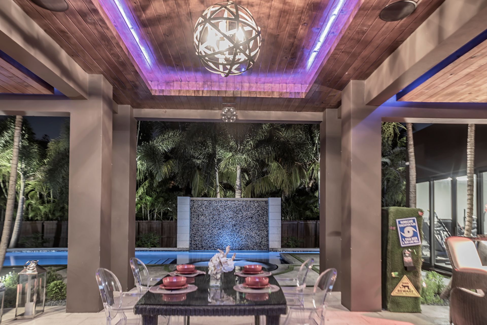 Outdoor dining area with a table set for a meal, a water feature, and a colorful illuminated ceiling.