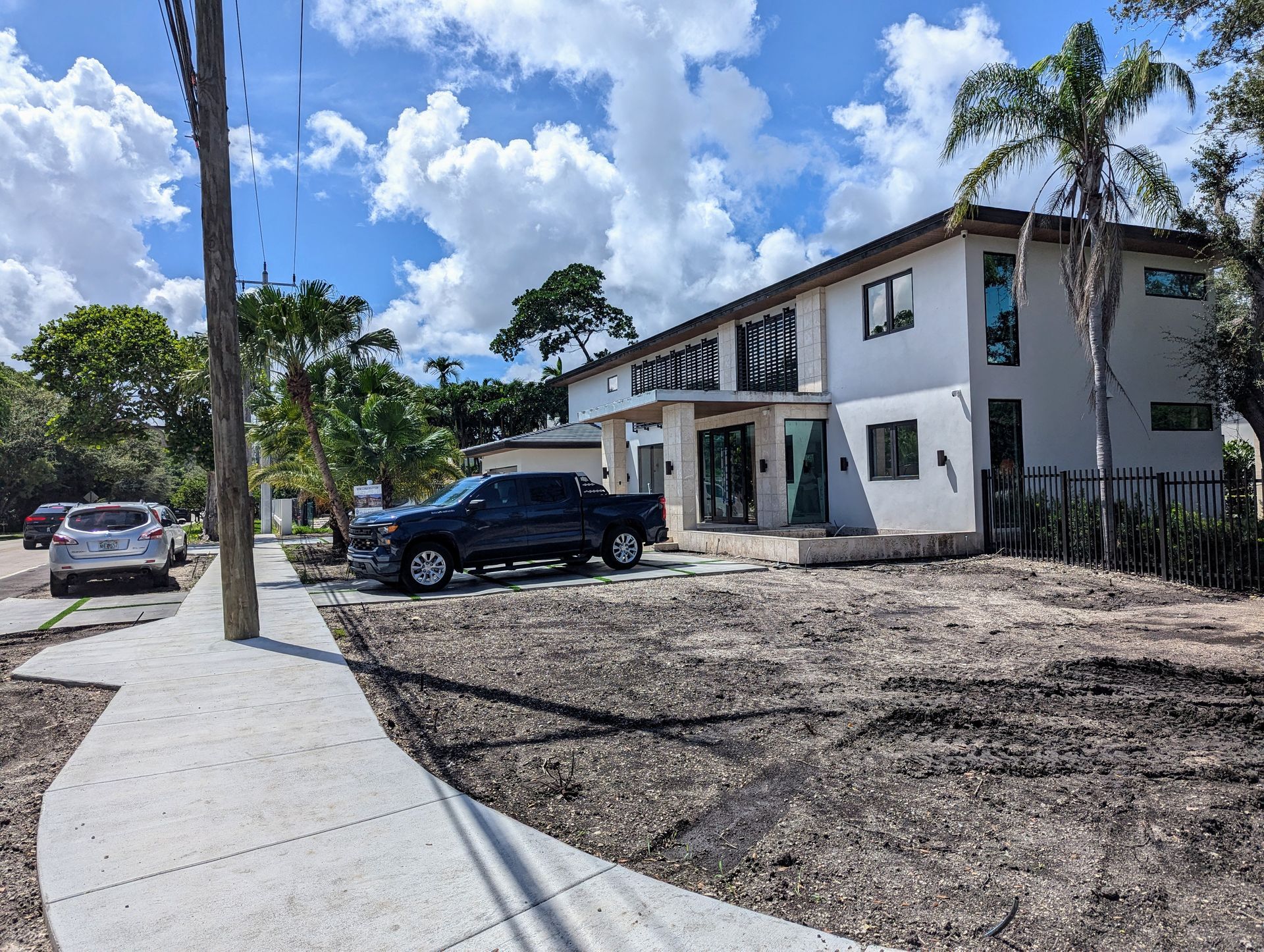 Modern two-story house with a black truck parked out front. Cloudy sky. Brown earth in the yard.