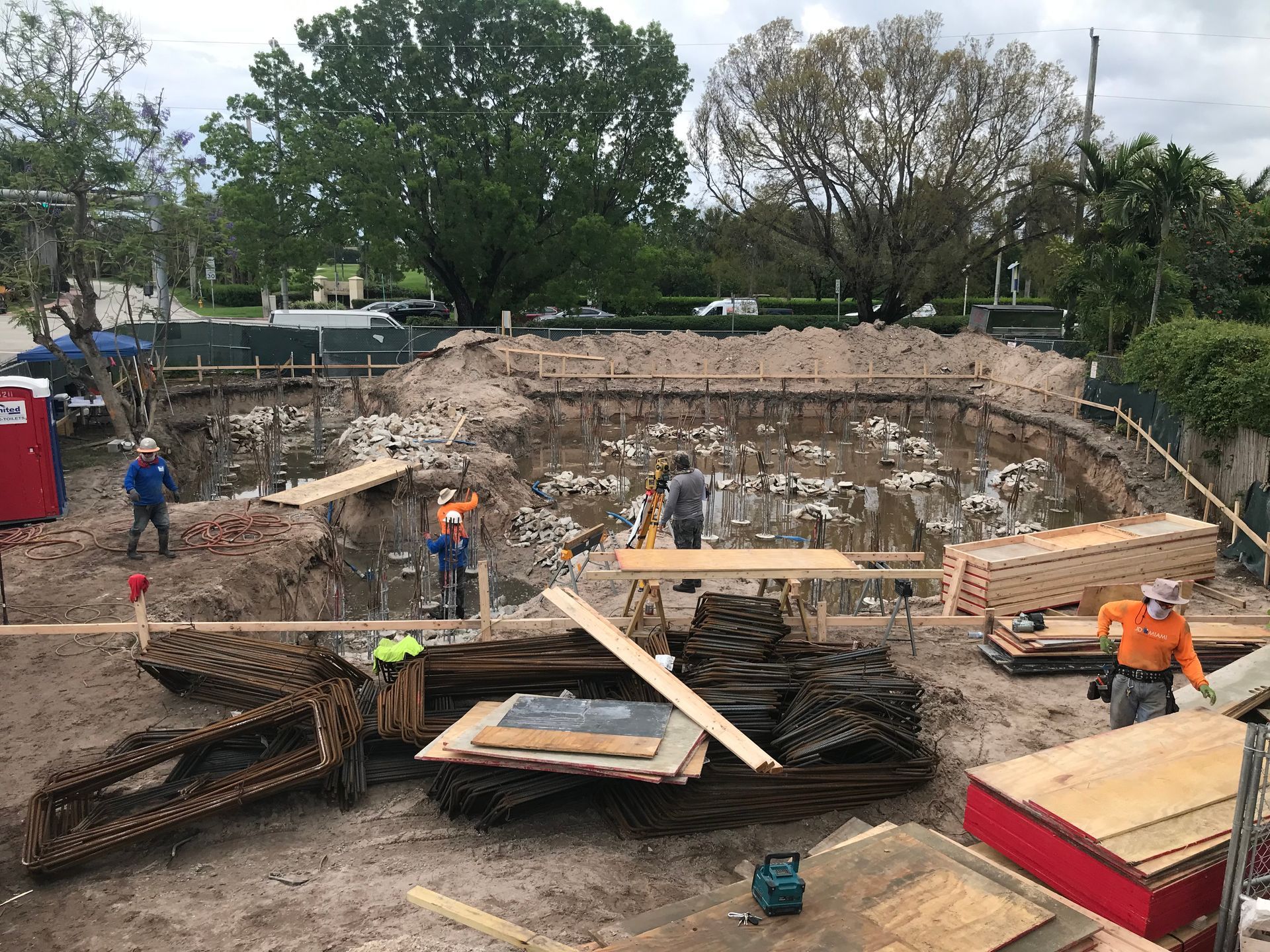 Construction site with workers in a large excavated area surrounded by wooden forms and equipment.