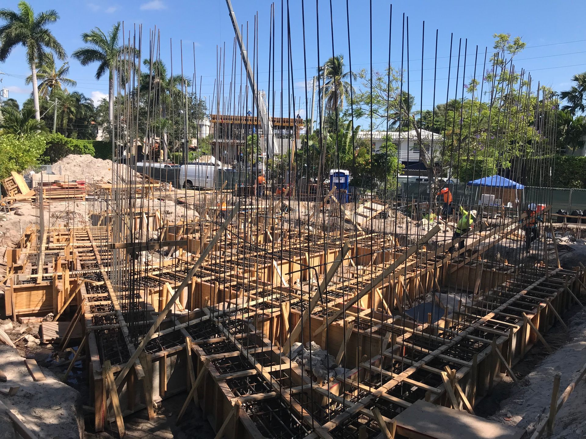 Construction site with wooden framework, steel rebar, and workers under blue sky.