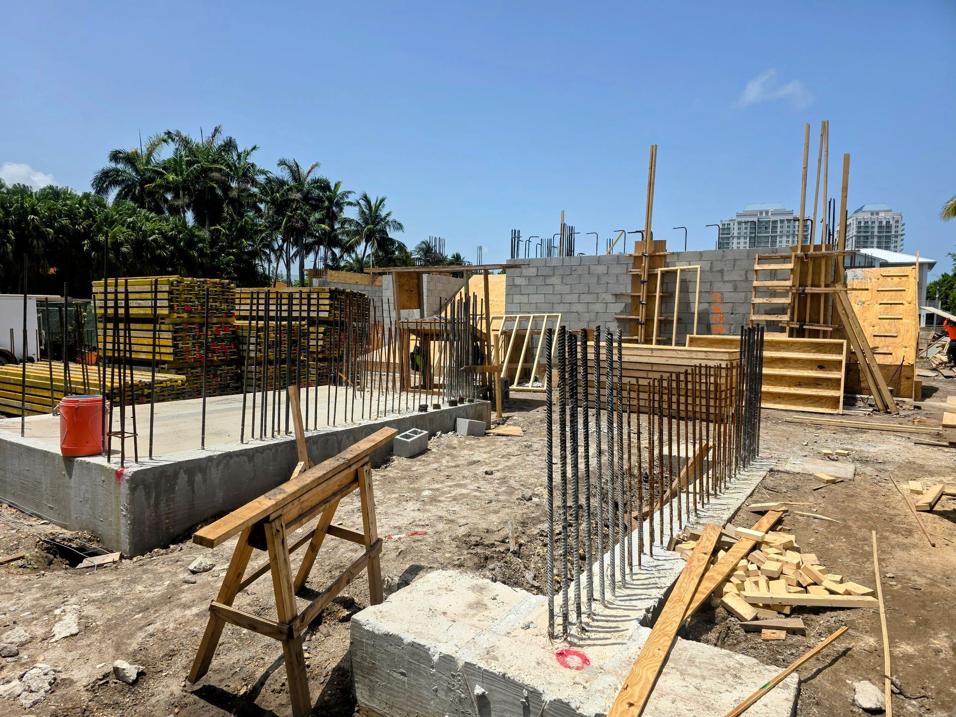Construction site with concrete foundations, rebar, and wooden framing under a blue sky.