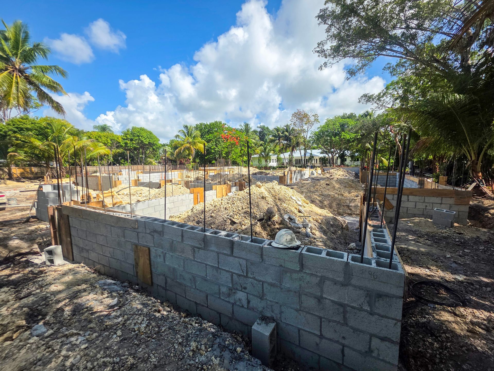 Construction site with cinder block walls, dirt, and concrete forms under a blue sky.