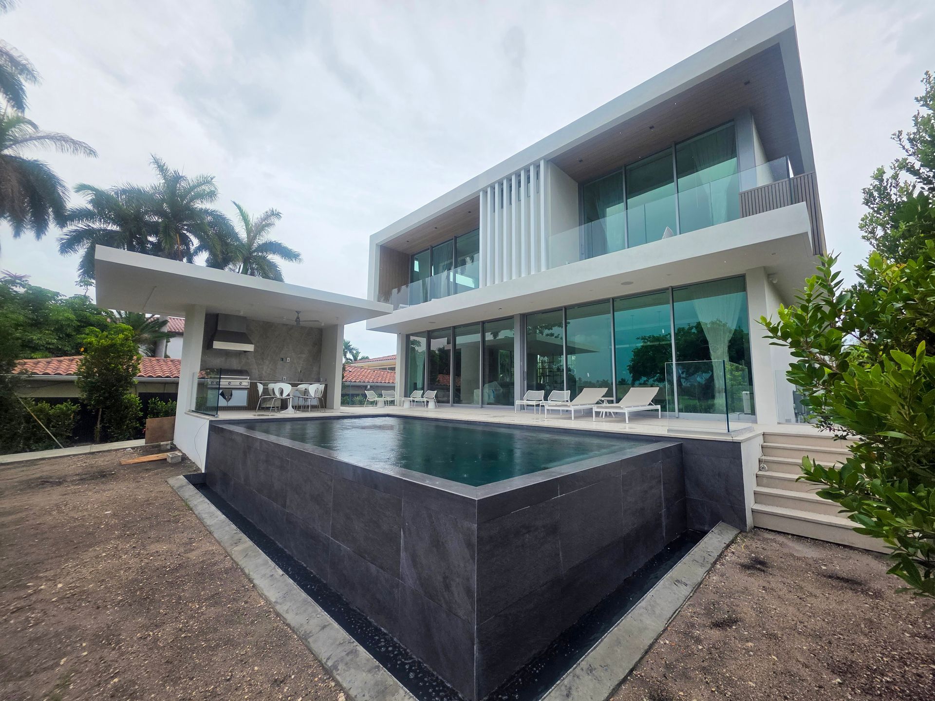 Modern white house with a pool and glass windows, overlooking the water.