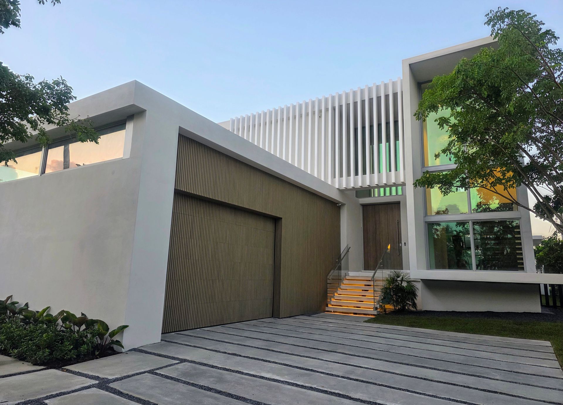 Modern white house with wood garage door, slatted facade, and multi-colored glass windows.