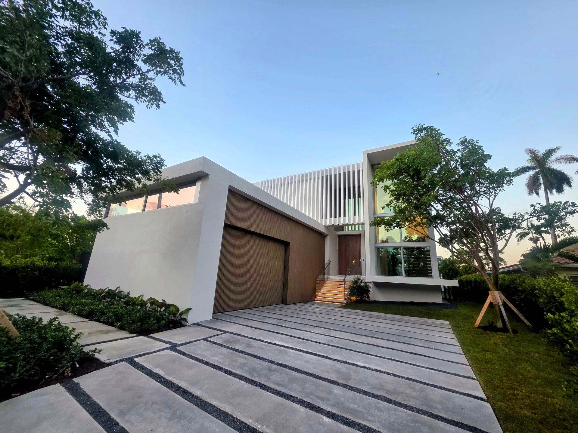 Modern white house with a wood garage door, slatted facade, and patterned driveway.