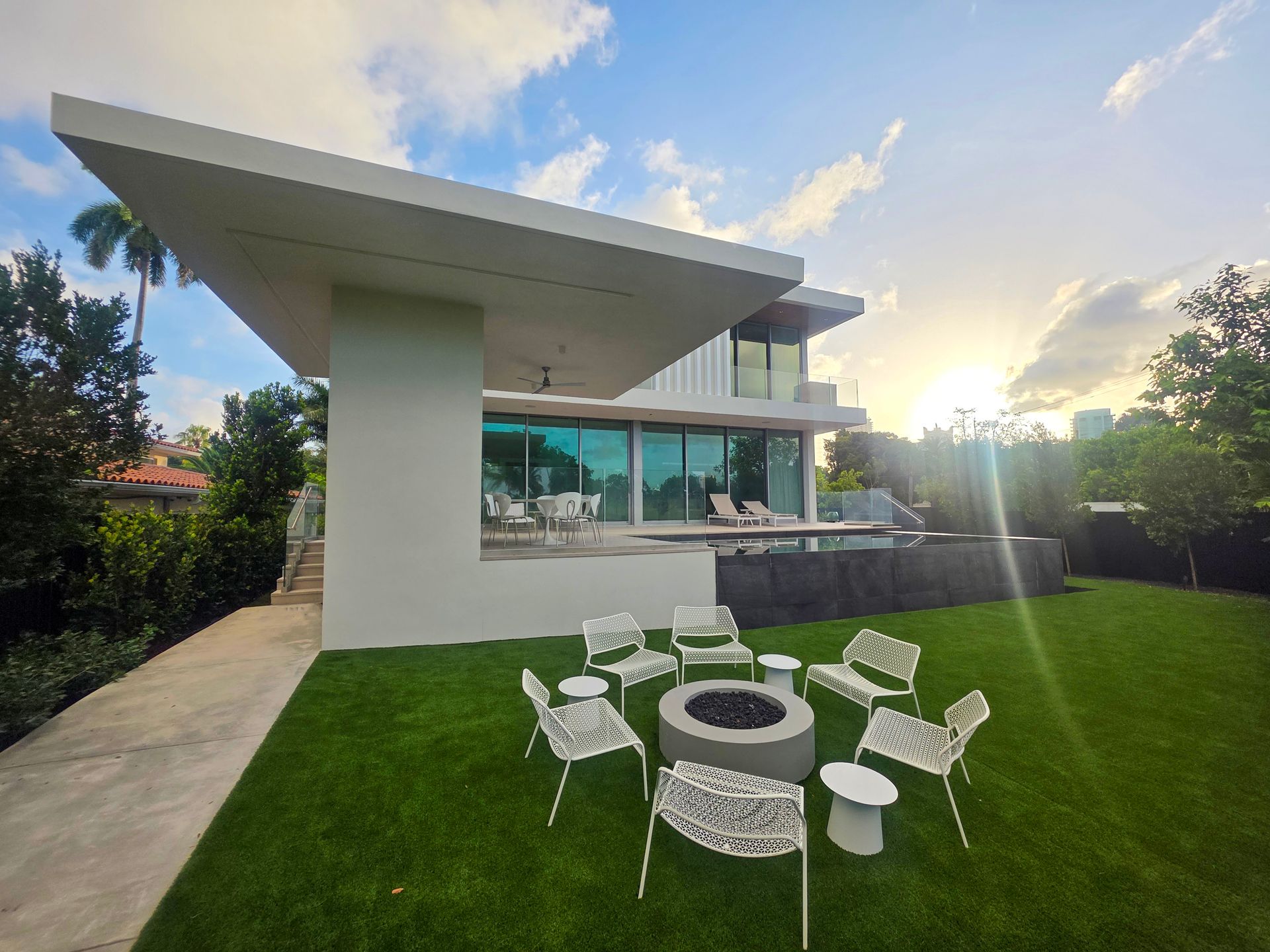 Modern white house with outdoor seating area, fire pit, and sunny lawn.