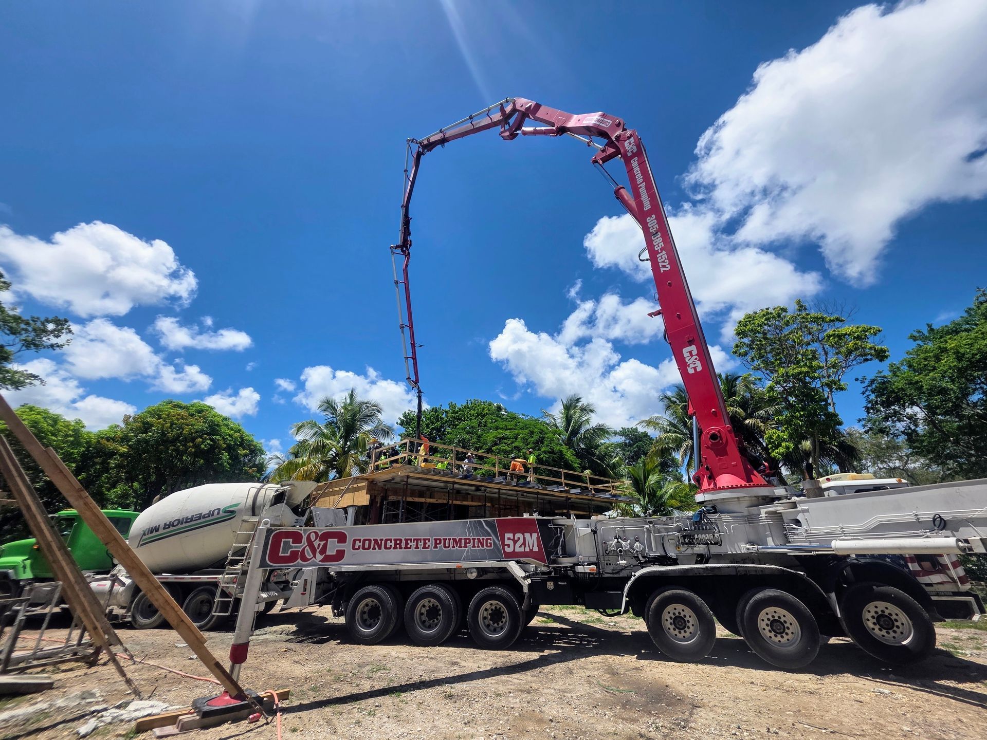 Concrete pump truck pouring concrete at a construction site. Red boom arm, blue sky.