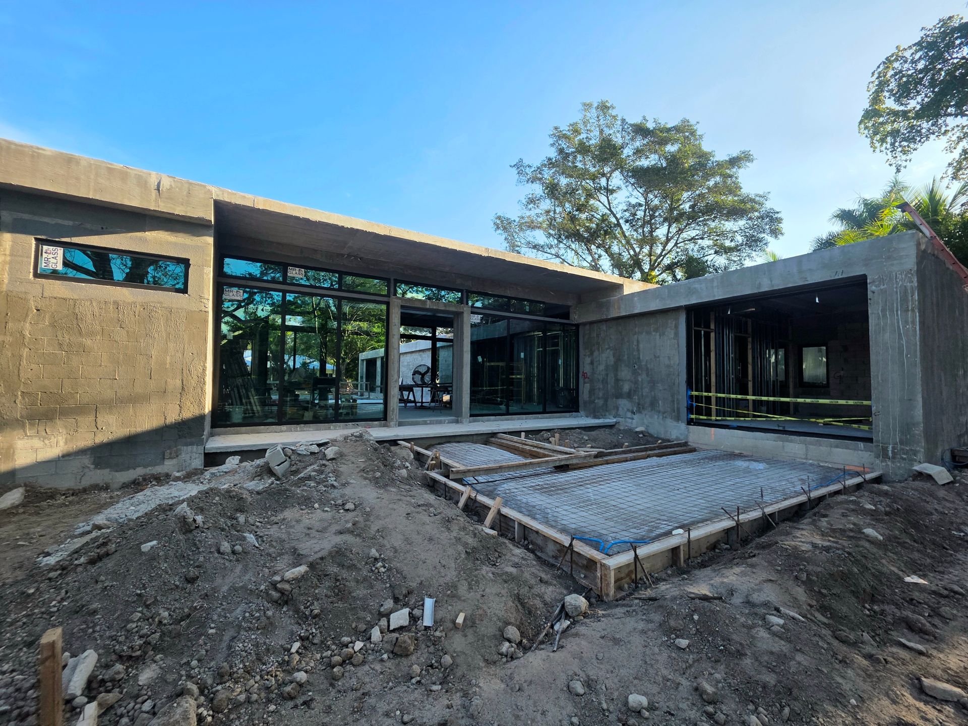 Concrete-framed modern house under construction; front view with large glass windows and concrete foundation.
