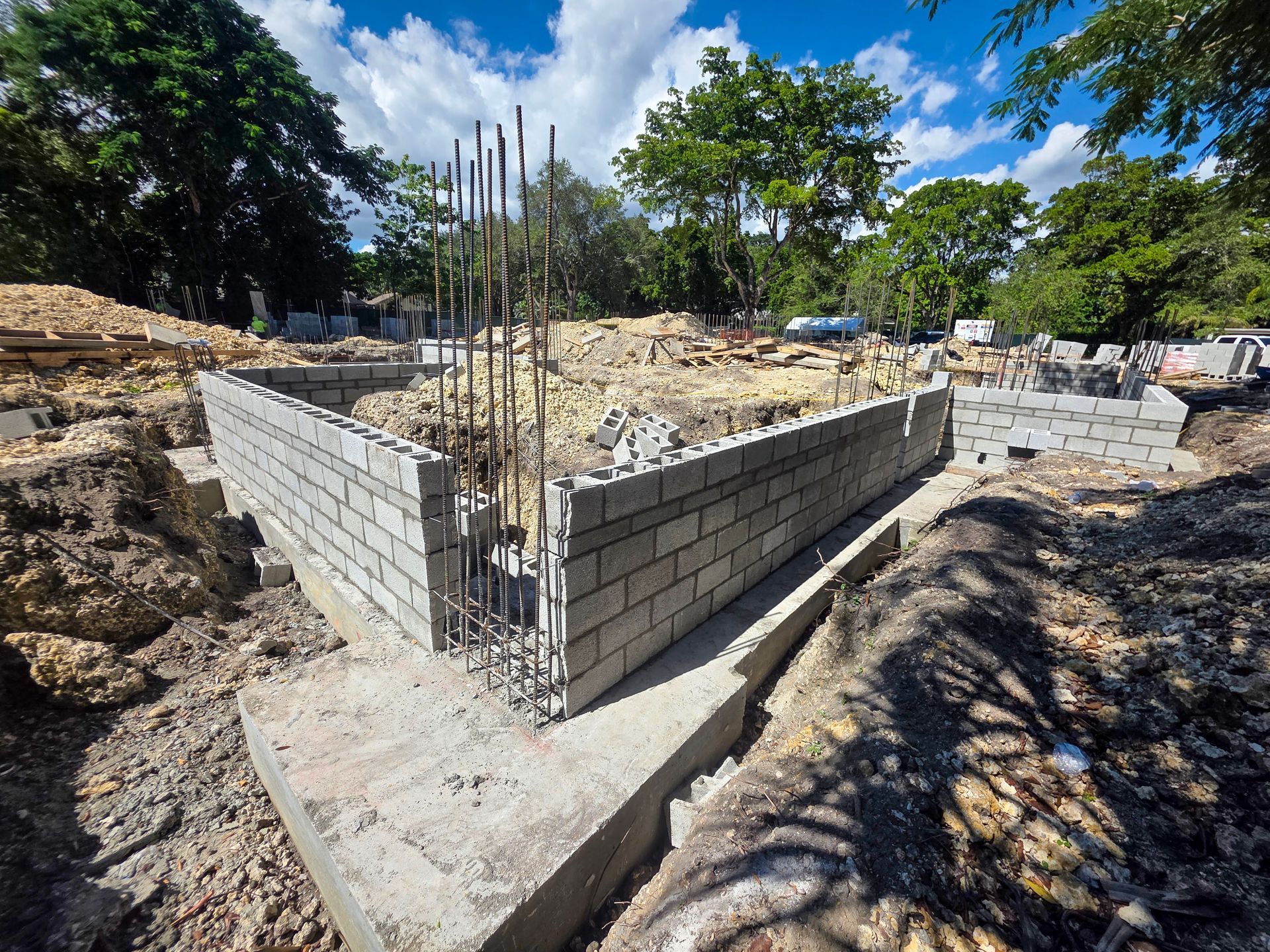 Construction site: foundation of a building made of gray concrete blocks. Steel rebar upright. Cloudy blue sky.