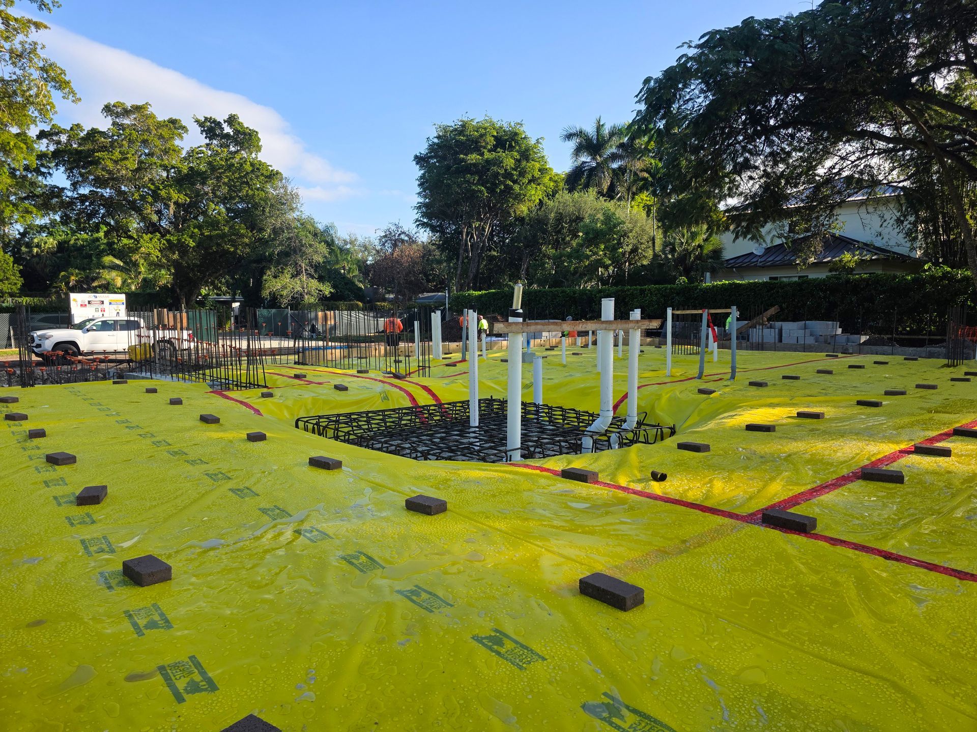 Construction site with yellow ground cover, bricks, and concrete pillars, under a sunny sky.