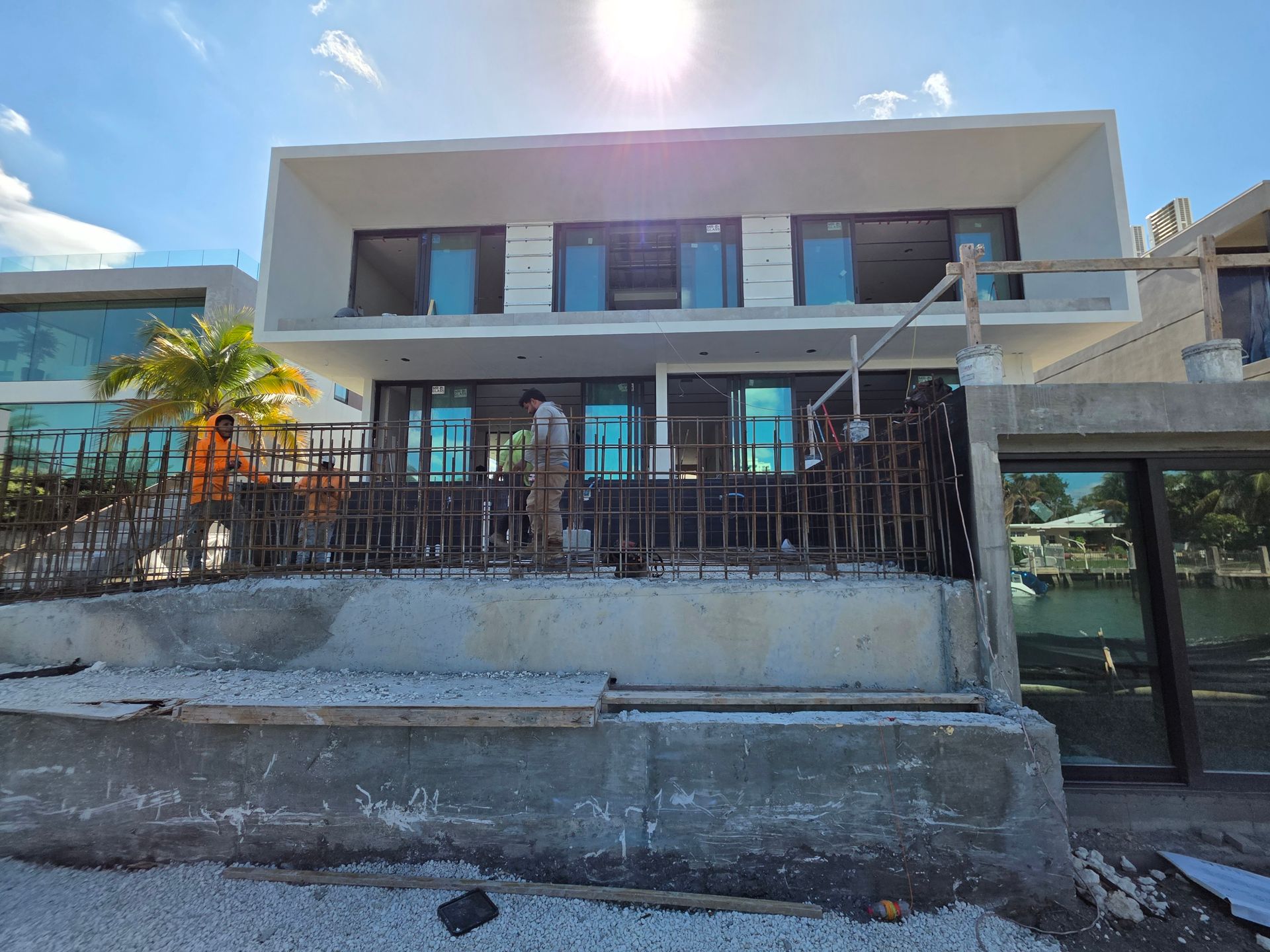 Two-story modern building under construction with glass windows and a concrete facade, bright sunlight.